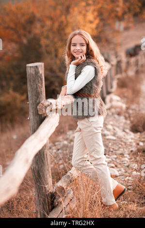 Beautiful blonde teen girl 13-14 year old wearing stylish clothes posing in autumn park. Looking at camera. Stock Photo