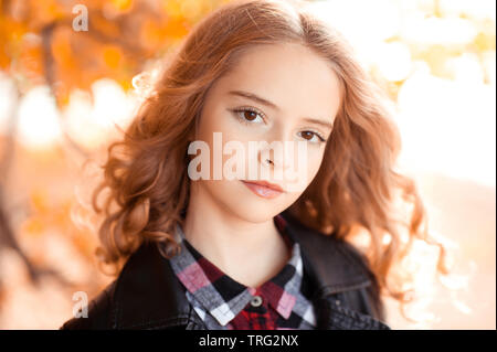 Beautiful blonde girl with long curly hair 12-14 year old wearing stylish jacket outdoors over autumn nature background. Looking at camera. Stock Photo