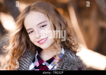 Portrait of teenage blonde girl 14-15 year old with long curly hair outdoors. Looking at camera. Stock Photo