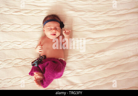 Cute baby girl wearing knitted clothes. Lying on bed with white knitted cover. Top view. Sleeping. Bedtime. Stock Photo
