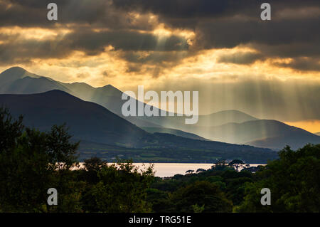 Crepuscular rays and shafts of sunlight streaming through gaps in dramatic clouds over Carrauntoohil and Macgillycuddy's Reeks, County Kerry, Ireland Stock Photo
