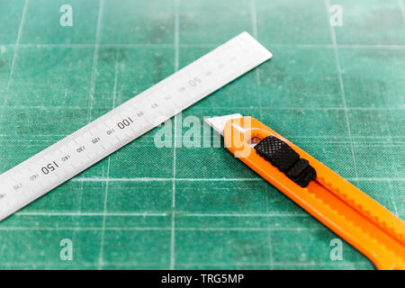 Stanley knife & ruler placed on top of old green cutting board. Stock Photo