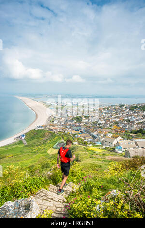 Jogger runs down steep path from Portland heights on the Isle of Portland towards Chesil Beach and the viilage of Fortuneswell, Dorset, England, UK. Stock Photo
