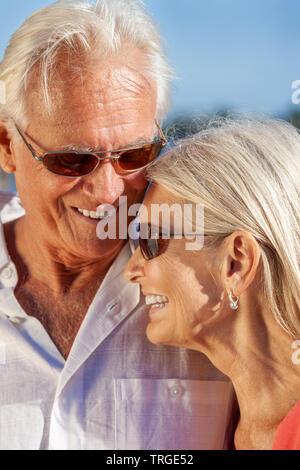 Happy senior loving man and woman romantic couple together outside in sunshine laughing wearing sunglasses Stock Photo