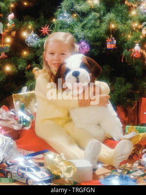 Christmas toys under the tree Young girl hugging toy dog Stock Photo