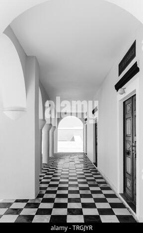 Portico of a church in Oia Santorini with black and white checkerboard tiles and white walls. Stock Photo
