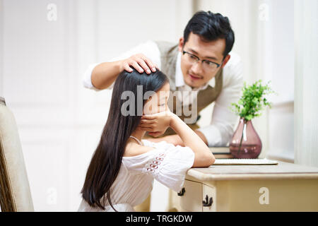 sad little asian girl sitting at desk in her room and getting comfort from caring father Stock Photo