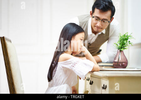 sad little asian girl sitting at desk in her room and getting comfort from caring father Stock Photo