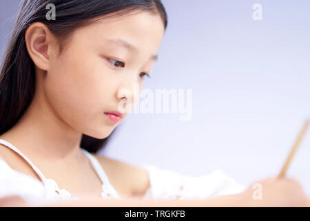 face of a little asian girl with long black hair writing or drawing, close-up shot. Stock Photo