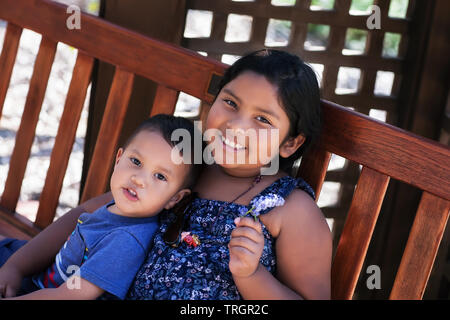 Two siblings, a young boy and older sister, sitting peacefully together on a bench. Stock Photo