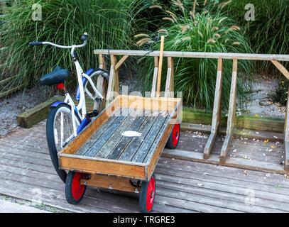 A cruiser bicycle and a wooden wagon are parked in a wooden bike rack in front of a summer home in Fire Island Long Island New York. Stock Photo