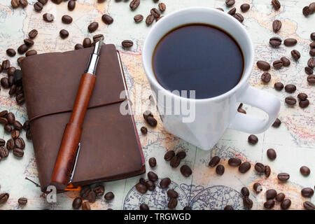 Opened Conklin Endura fountain pen with a small leather traveler's notebook on a map with scattered coffee beans and a white filled coffee cup. Stock Photo