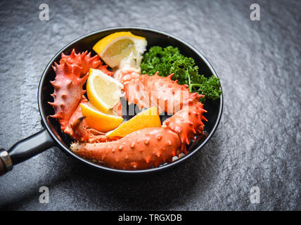 Boiled crab claws cooked seafood pan with Alaskan King Crab with lemon parsley herbs and spices on dark background / red crab hokkaido in a hot pot Stock Photo