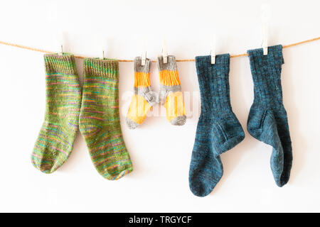 Several pairs of colorful woolen socks of various sizes hanging on a rope with white background Stock Photo