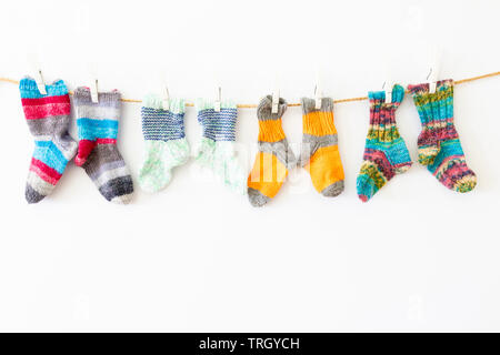 Several pairs of colorful woolen socks of various sizes hanging on a rope with white background Stock Photo