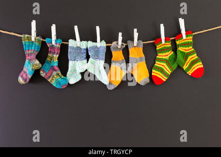 Several pairs of colorful woolen socks of various sizes hanging on a rope with red background Stock Photo