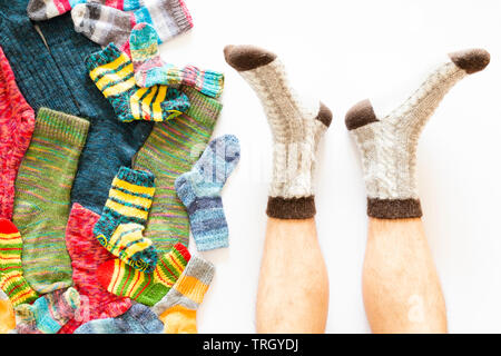 Top view of an assortment of colorful woolen socks of various sizes on white background with a pair of feet wearing gray brown socks Stock Photo