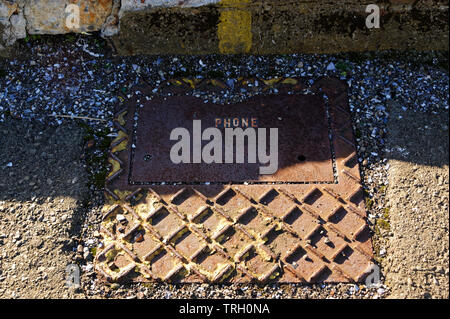 An old, solid, patterned iron phone cover on the ground, it has the word PHONE in yellow painted on it Stock Photo