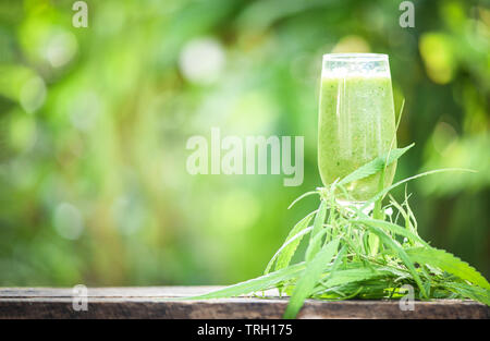 summer juice with green fruit smoothies in glass with cannabis leaf marijuana plant on wooden table green background / cannabis food Stock Photo