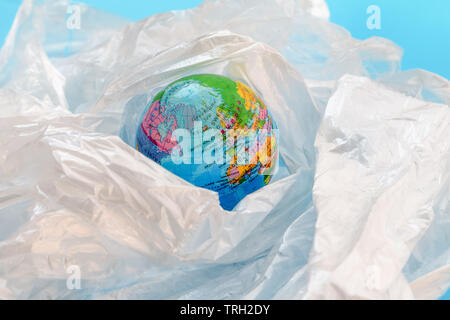 Concept of the plastic pollution problem in the world.  The planet earth is floating around in a soup of white plastic bags on against blue background Stock Photo