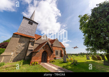 Airliner jet plane taking off from London Southend Airport, Southend on Sea, Essex, UK passing St Laurence & all saints church, trees and gravestones Stock Photo