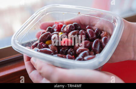 Kalamata or Kalamon purple Greek olives contained in a plastic tray held by two hands. Fresh aperitif, with olive oil and slightly spicy Stock Photo