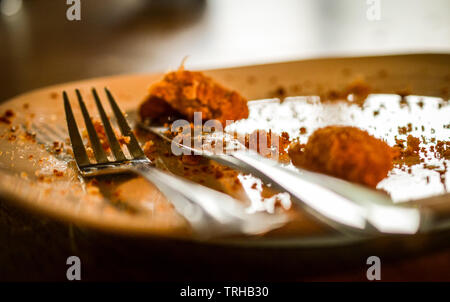 A knife and fork on an empty plate with leftover food on it and crumbs Stock Photo