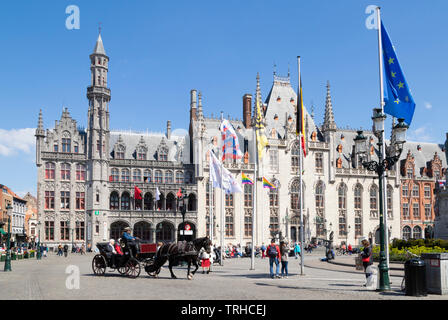 Tourists touring Bruges in a horse drawn carriage going past the Provincial Court Provinciaal Hof in the Markt central Bruges Belgium EU Europe Stock Photo