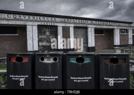 An abandoned toilet block, decaying with age, with four recycling bins in the foreground, also in poor condition, located in Barry Island, Barry, Wale Stock Photo