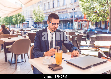 Handsome man in glasses working with smartphone and documents at outdoor cafe Stock Photo