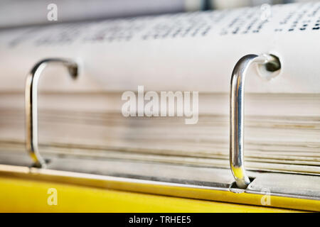 Open yellow binder close up , stack of white papers and bright metal rings , in the background black text out of focus Stock Photo