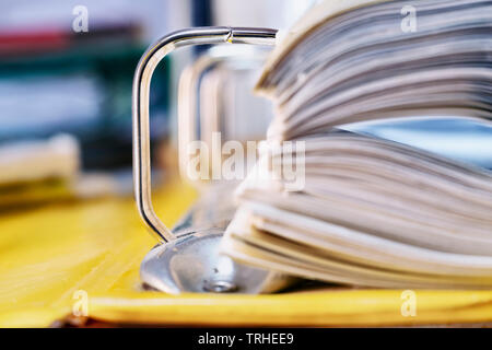 Open yellow binder close up , stack of white papers and bright metal rings , in the background office folders Stock Photo