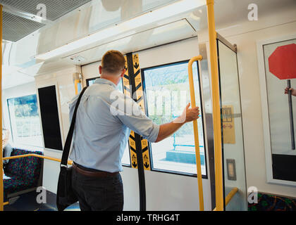 A rear-view shot of a mid-adult businessman standing on a train commuting to work, he is arriving at his destination. Stock Photo
