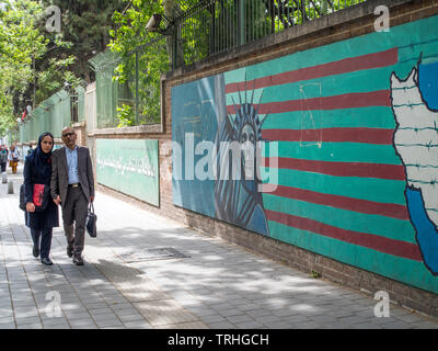 Pedestrians walk past a painting of the Statue of Liberty as a skeleton outside the former United States embassy in Tehran. Stock Photo