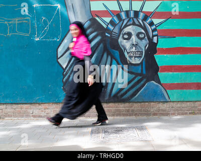 A pedestrian walks past a mural depicting the Statue of Liberty as death as painted on the wall of the former American Embassy in Tehran, Iran. Stock Photo