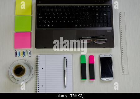 laptop, cup of coffee, smartphone, sticker, pen, notepad and glasses lying on the table Stock Photo