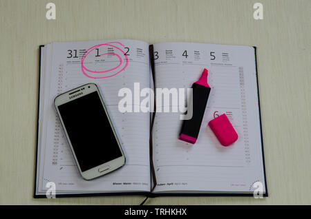open diary with marked date, mobile phone and red marker Stock Photo