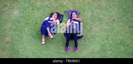 Two young women lying on the lawn gazing up to the sky, at Gardens by the Bay Singapore. Stock Photo