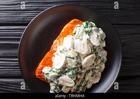 Florentine Salmon is simmered in a creamy wine sauce and topped with sauteed spinach and mushrooms close up on the plate on the table. Horizontal top Stock Photo
