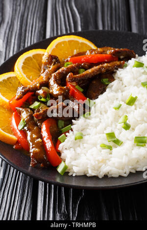 Fried sliced beef steak with bell pepper in soy orange sauce served with rice closeup on a plate. vertical Stock Photo