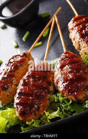 Tsukune are tender ground chicken skewers with bits of shiso leaves and scallions, drizzled with sweet soy sauce closeup on a plate. vertical Stock Photo