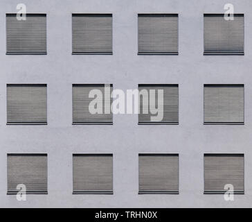 Abstract and minimalist view on the grey wall of an office building in the hard and hot summer sunlight with all the silver roller blinds shut Stock Photo