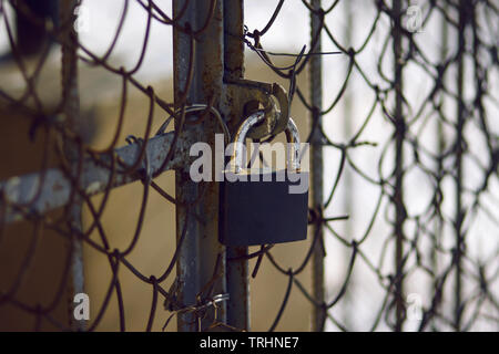Old, scratched and rusty from time to time padlock closes the metal gate with a mesh fence Stock Photo
