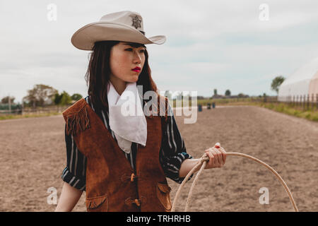 pretty Chinese cowgirl throwing the lasso in a horse paddock on a wild west farm Stock Photo