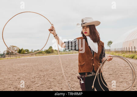 pretty Chinese cowgirl throwing the lasso in a horse paddock on a wild west farm Stock Photo