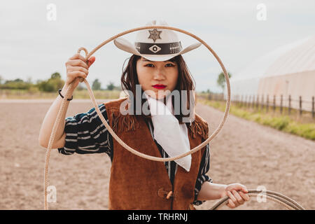 pretty Chinese cowgirl throwing the lasso in a horse paddock on a wild west farm Stock Photo