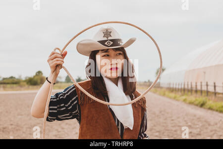 pretty Chinese cowgirl throwing the lasso in a horse paddock on a wild west farm Stock Photo