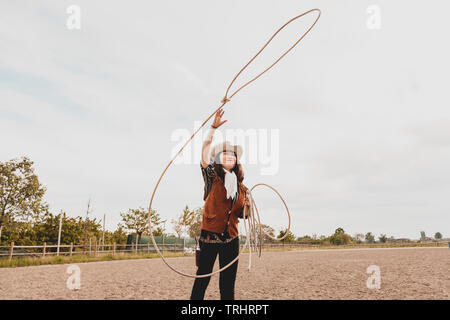 pretty Chinese cowgirl throwing the lasso in a horse paddock on a wild west farm Stock Photo