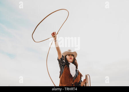 pretty Chinese cowgirl throwing the lasso in a horse paddock on a wild west farm Stock Photo