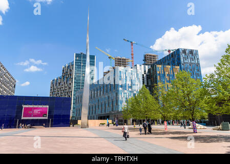 London, UK - May 1, 2018: People visit Peninsula Square with modern buildings with shops, bars and restaurants in front of the O2 Arena Stock Photo